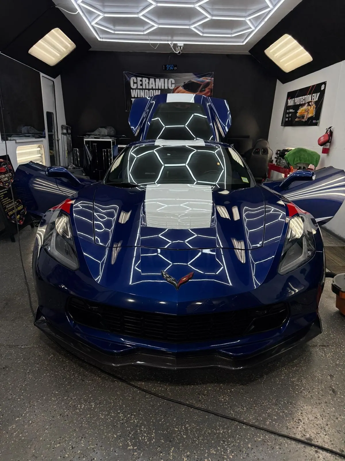 A Chevrolet Corvette on the Custom Auto Care shop floor under the hexagon lighting rig