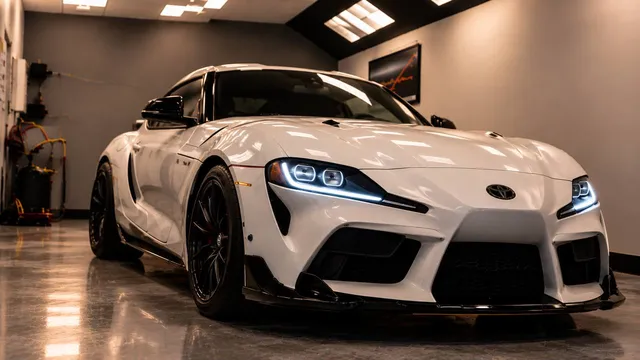 A white Toyota Supra with its headlights on inside the Custom Auto Care bay